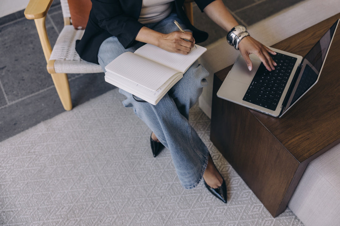Image of faceless woman working on a laptop with a notebook on her lap and a pen in her hand. She is wondering if it is too late to begin selling digital products. 
